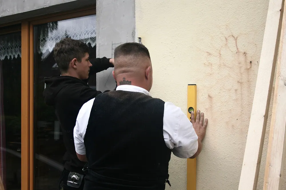 Zwei Zimmerer richten eine Latte an einer Hauswand mit der Wasserwaage aus